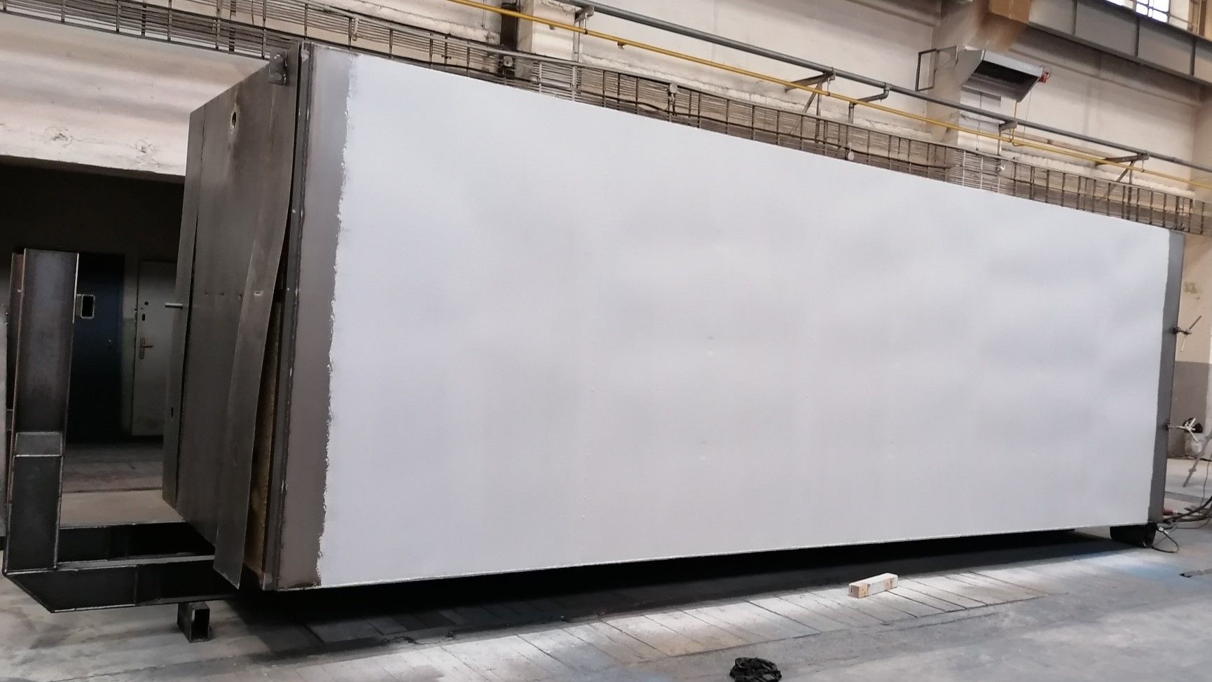 Boční stěna velkého kontejneru nastříkaná světle šedou základovou barvou v lakovně. Okraje konstrukce a spodní rám jsou zatím v původní tmavé barvě kovu.