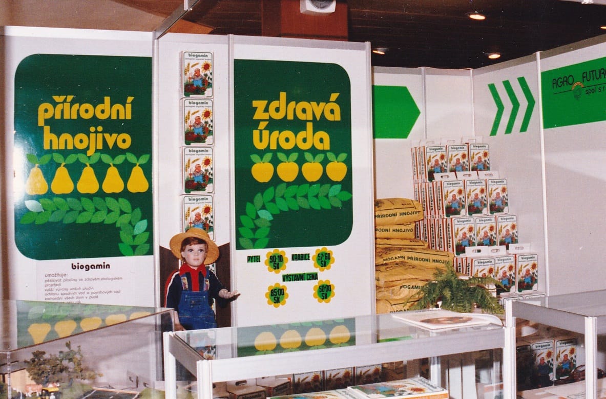 Dobová fotografie výstavního stánku propagujícího přírodní hnojivo Biogamin. Stánek je zdoben zelenými panely s nápisy „přírodní hnojivo“ a „zdravá úroda“, vystavenými krabicemi produktu a figurínou chlapce v klobouku.